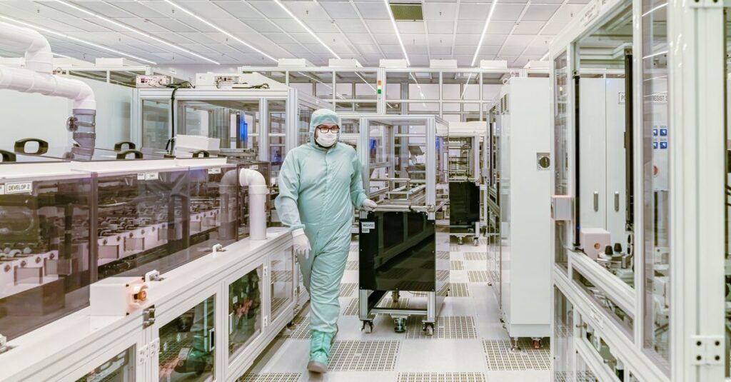 Scientist in protective gear walking in a high-tech cleanroom laboratory environment.