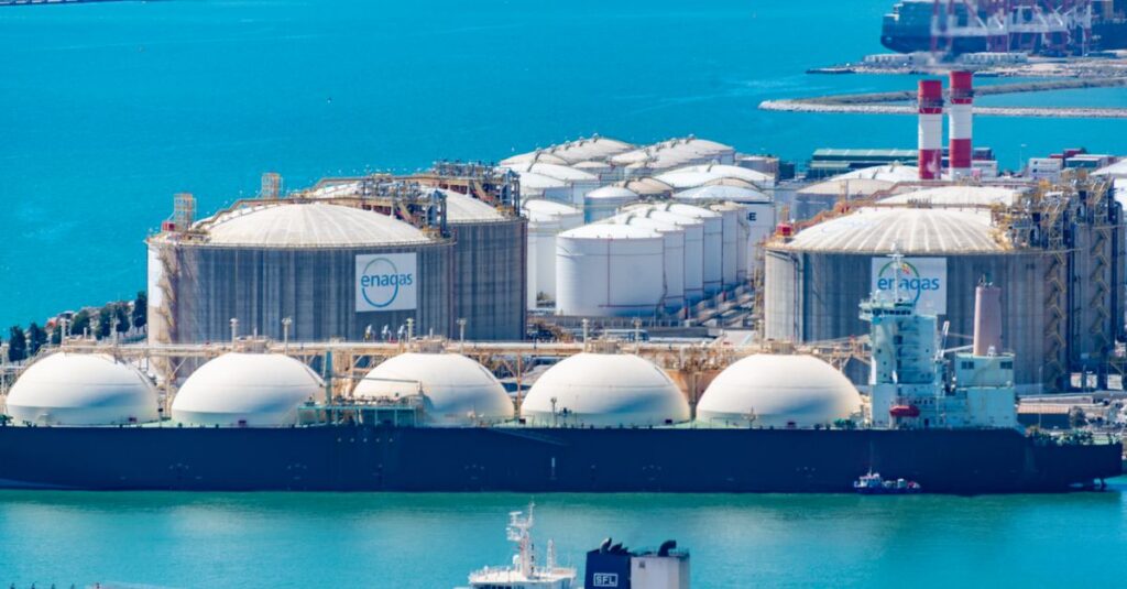 Aerial shot of a gas terminal featuring LNG storage tanks and tanker ships in turquoise waters.
